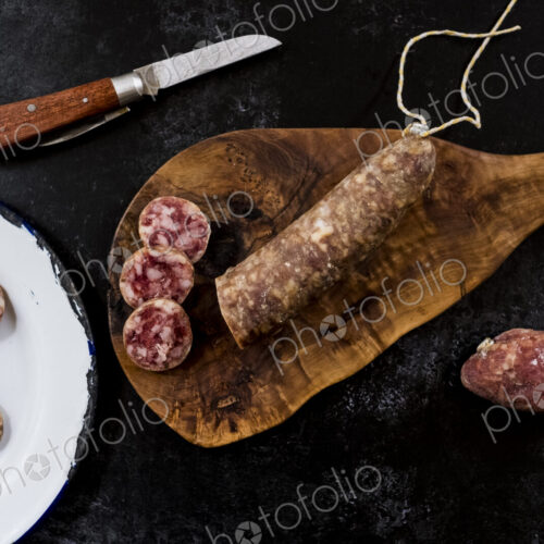 High angle close up of knife, sliced salami on wooden cutting board and white enamel… High angle close up of knife, sliced salami on wooden cutting board and white enamel…