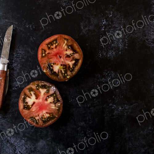 High angle close up of knife with wooden handle and fresh tomato cut in half and on… High angle close up of knife with wooden handle and fresh tomato cut in half and on…
