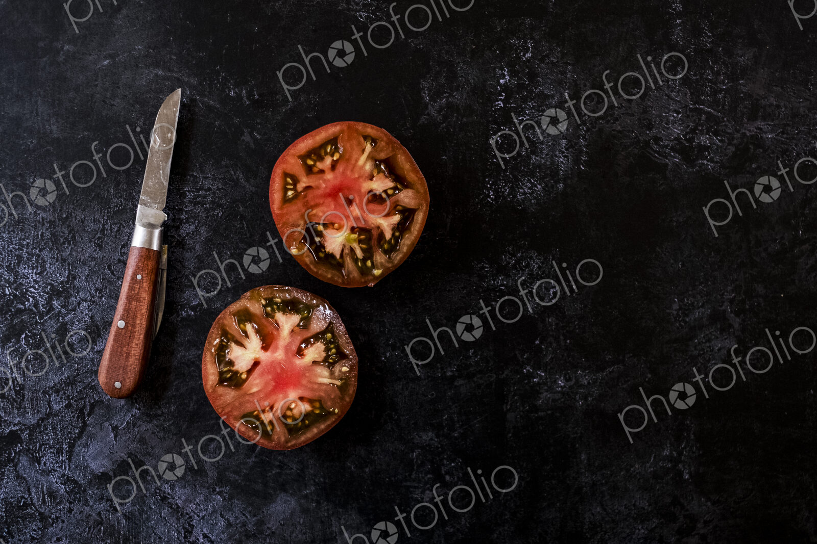 High angle close up of knife with wooden handle and fresh tomato cut in half and on…