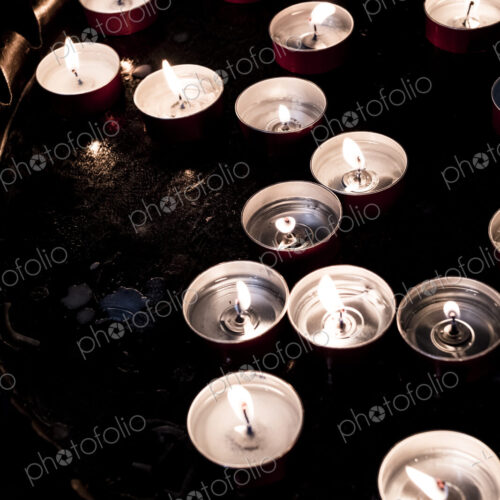 High angle close up of lit tea light candles on a tray in a church.
