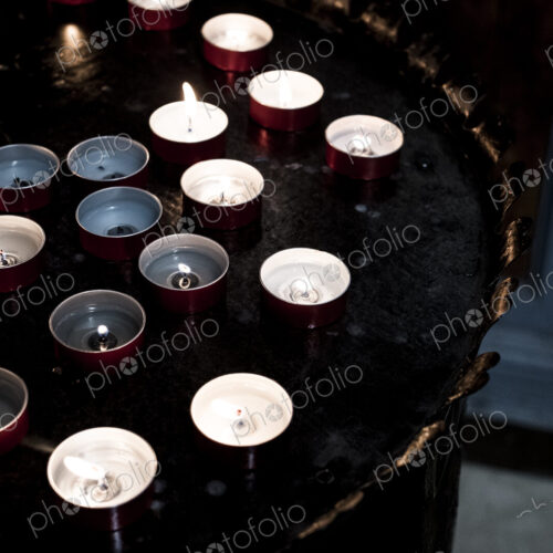 High angle close up of lit tea light candles on a tray in a church.