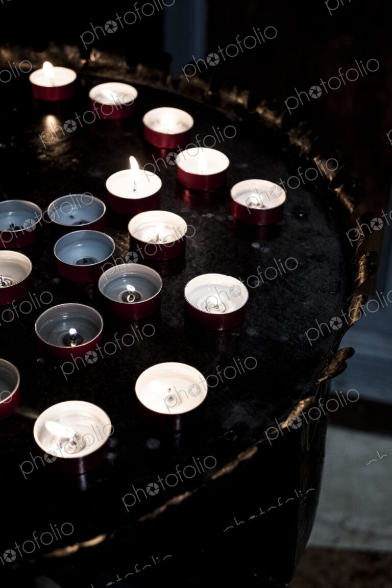 High angle close up of lit tea light candles on a tray in a church.