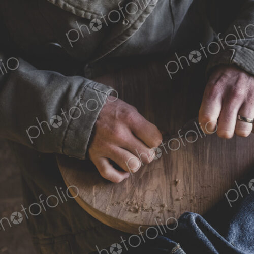 High angle close up of man sitting in workshop, holding piece of wood. High angle close up of man sitting in workshop, holding piece of wood.
