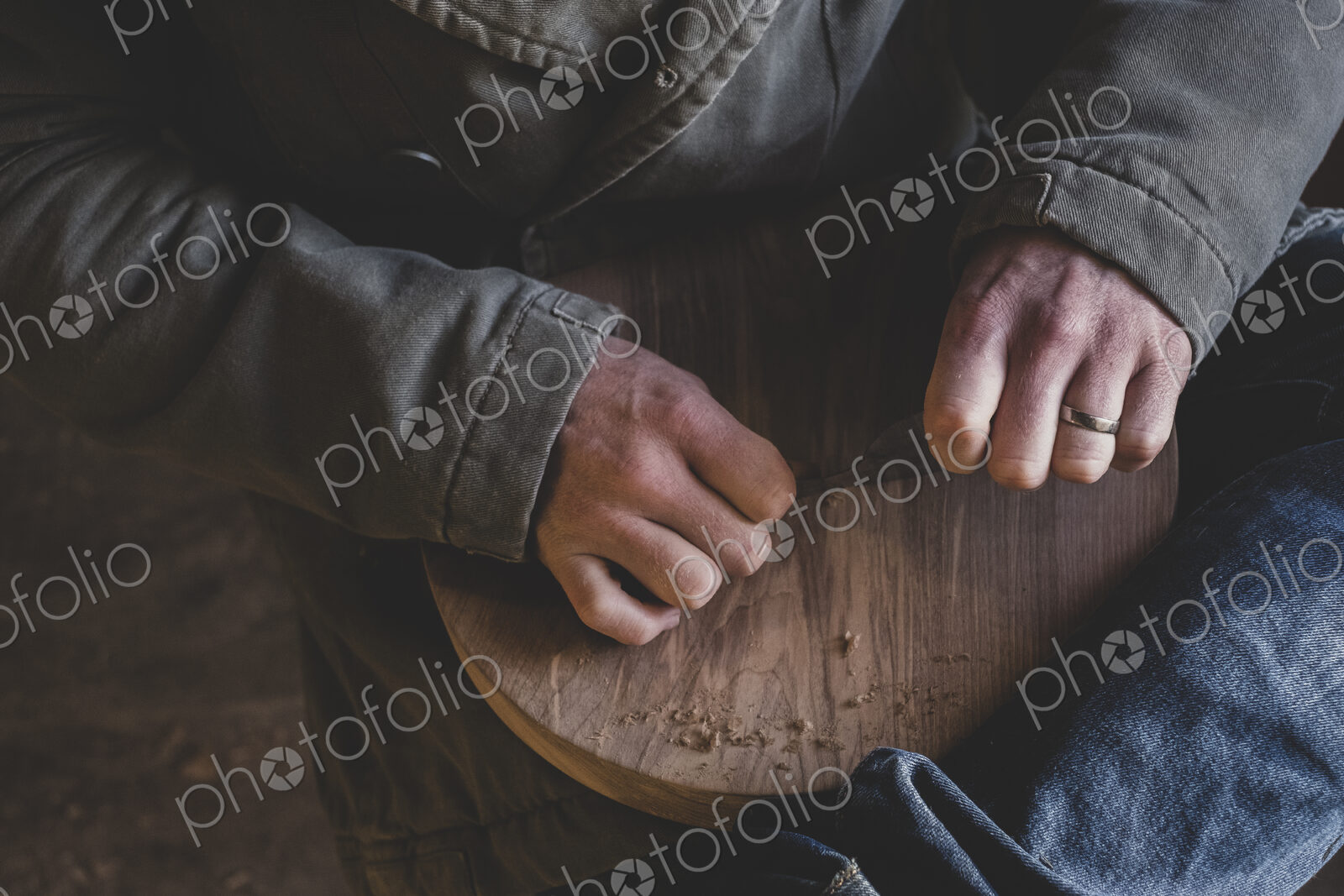 High angle close up of man sitting in workshop, holding piece of wood.