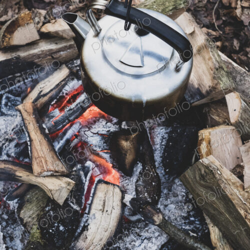 High angle close up of metal kettle hanging over a campfire.