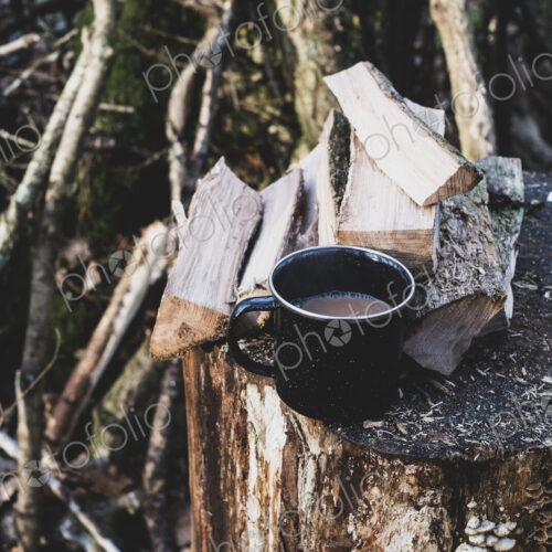 High angle close up of mug of tea and wooden logs on chopping block.