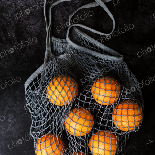 High angle close up of oranges in grey net bag on black background. High angle close up of oranges in grey net bag on black background.