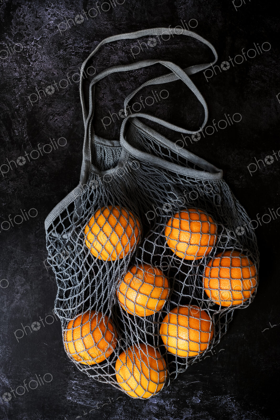 High angle close up of oranges in grey net bag on black background.