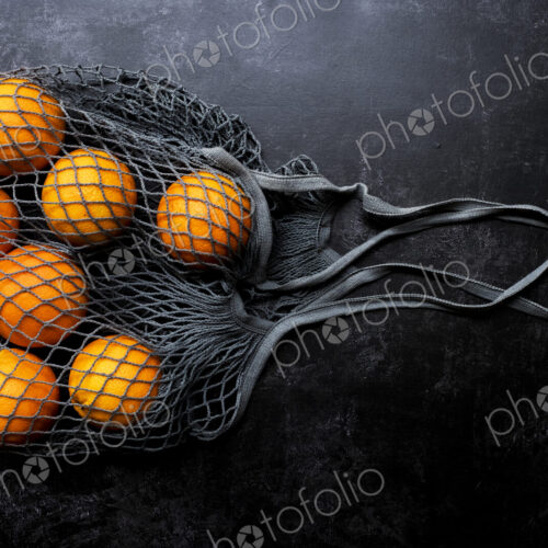 High angle close up of oranges in grey net bag on black background. High angle close up of oranges in grey net bag on black background.