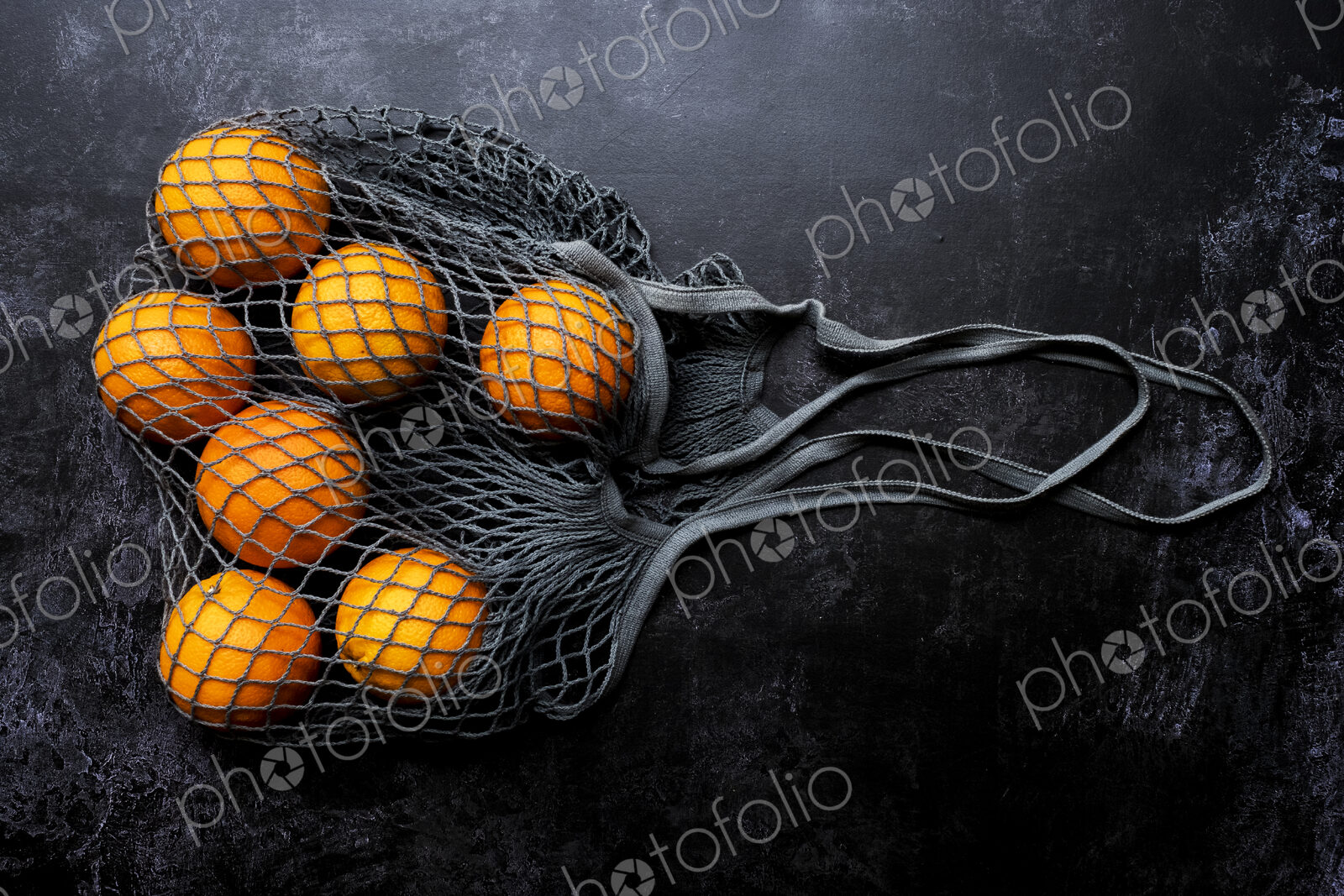 High angle close up of oranges in grey net bag on black background.