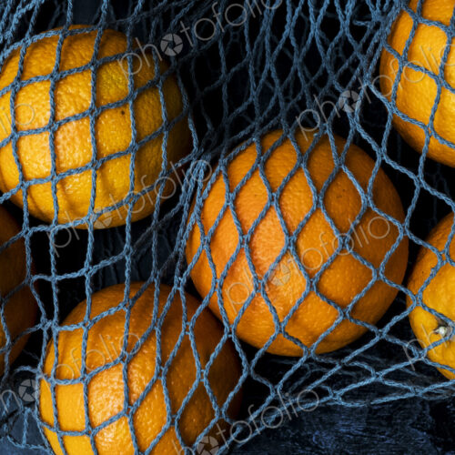 High angle close up of oranges in grey net bag on black background. High angle close up of oranges in grey net bag on black background.