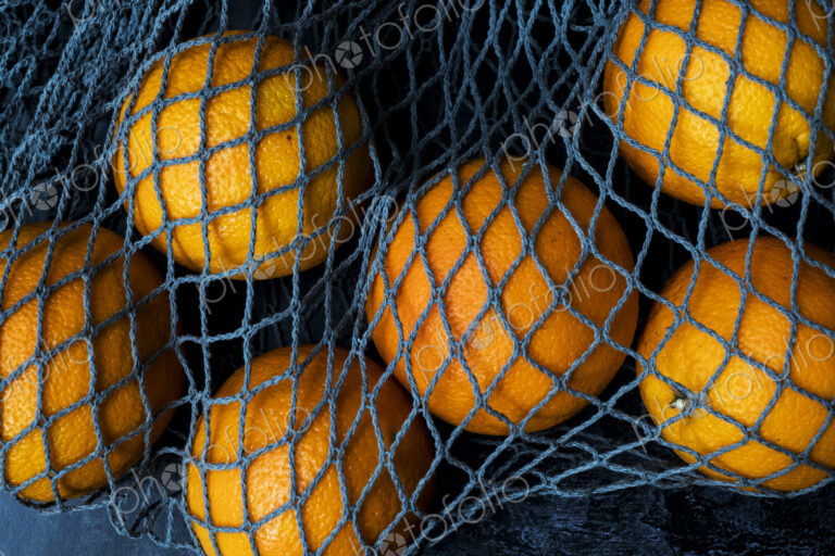 High angle close up of oranges in grey net bag on black background.