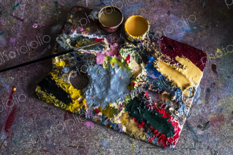 High angle close up of painter's palette, oil paints and paintbrush in a workshop.