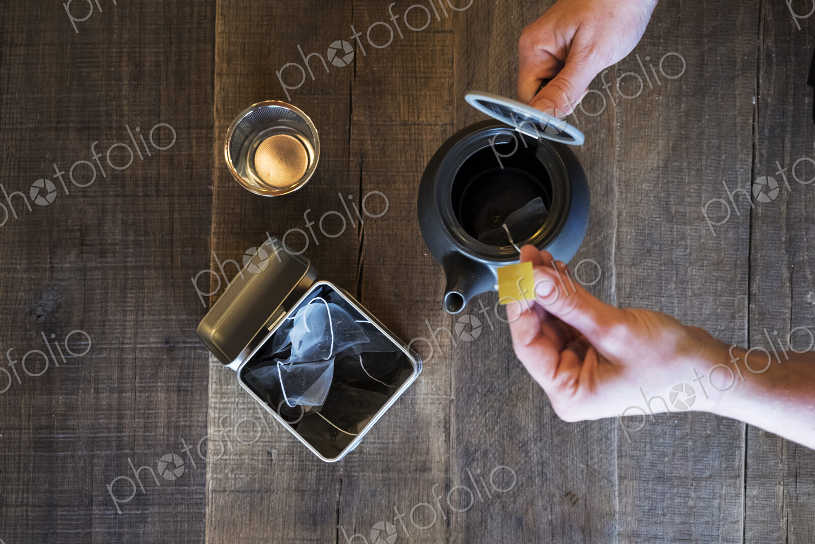 High angle close up of person adding tea bag to small black tea pot.