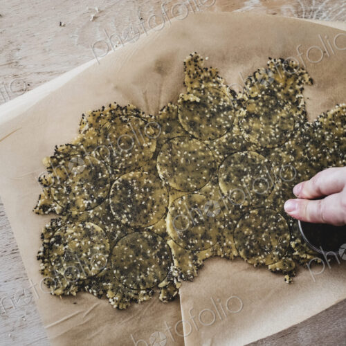 High angle close up of person cutting discs of seeded cracker dough.