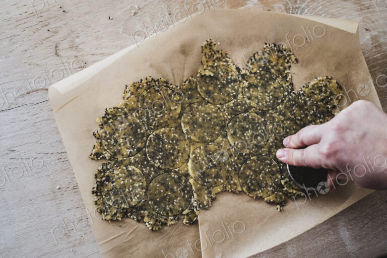 High angle close up of person cutting discs of seeded cracker dough.