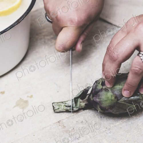 High angle close up of person cutting fresh artichoke with kitchen knife. High angle close up of person cutting fresh artichoke with kitchen knife.