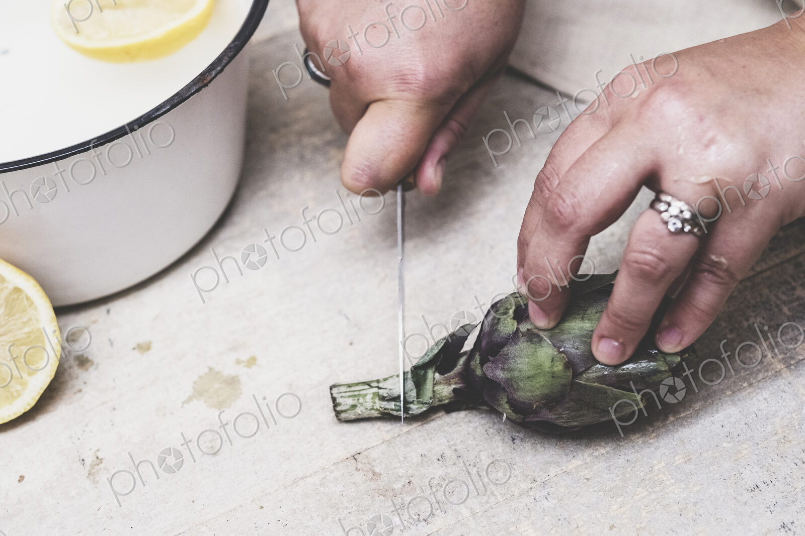 High angle close up of person cutting fresh artichoke with kitchen knife.