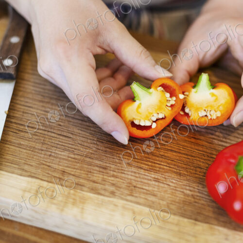 High angle close up of person cutting fresh red bell peppers on wooden cutting board. High angle close up of person cutting fresh red bell peppers on wooden cutting board.
