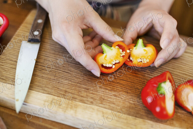 High angle close up of person cutting fresh red bell peppers on wooden cutting board.
