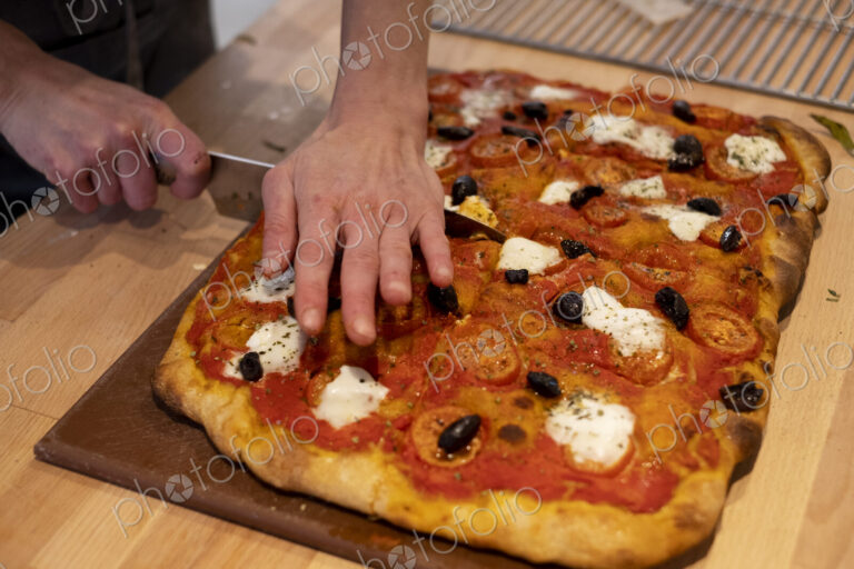 High angle close up of person cutting freshly baked pizza in an artisan bakery.