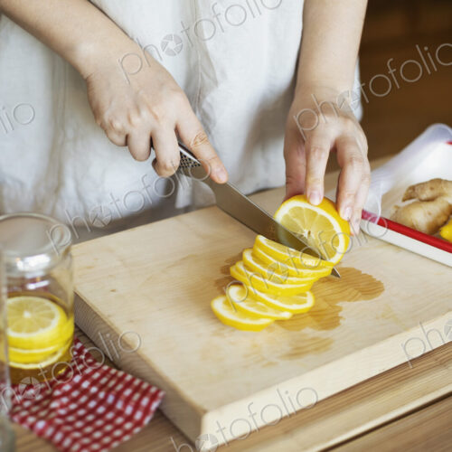 High angle close up of person cutting lemon with knife on wooden cutting board. High angle close up of person cutting lemon with knife on wooden cutting board.