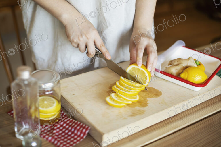 High angle close up of person cutting lemon with knife on wooden cutting board.