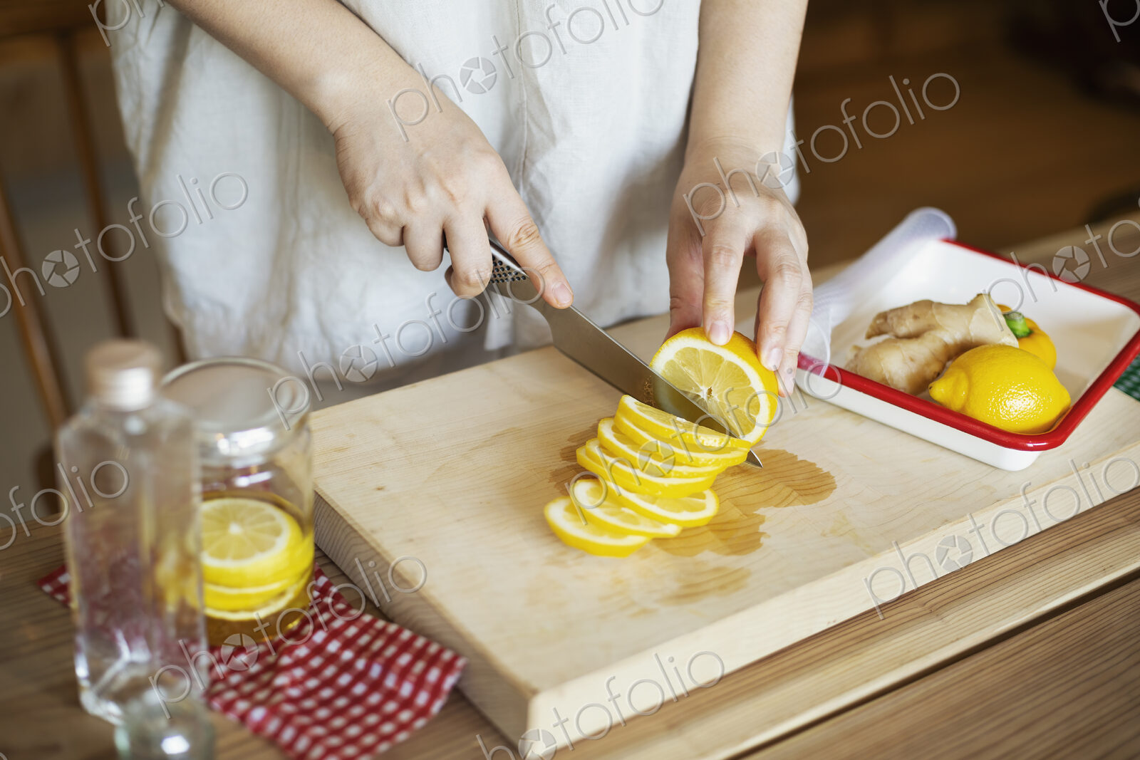 High angle close up of person cutting lemon with knife on wooden cutting board.