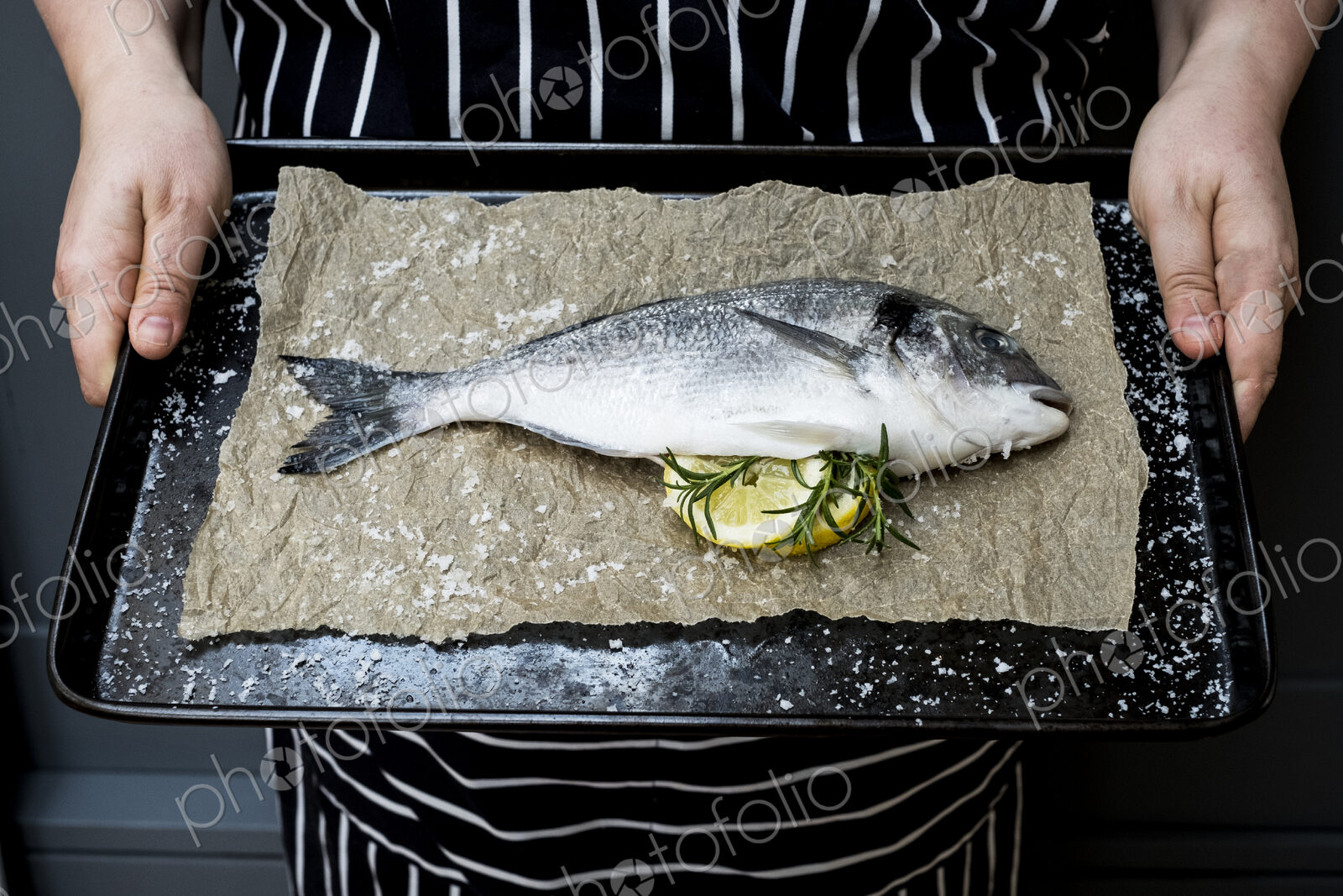 High angle close up of person holding baking tray with fresh sea bream, slices of…