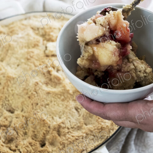 High angle close up of person holding bowl of freshly baked apple and blueberry crumble. High angle close up of person holding bowl of freshly baked apple and blueberry crumble.