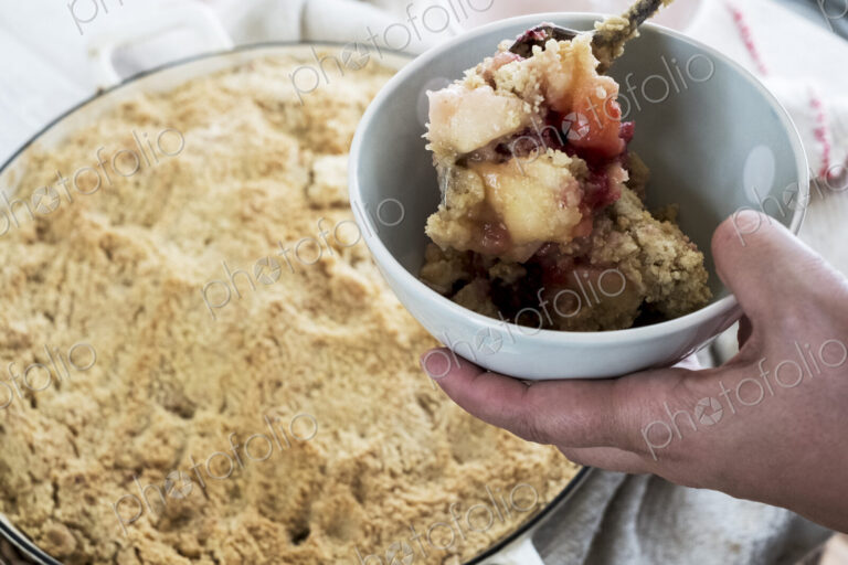 High angle close up of person holding bowl of freshly baked apple and blueberry crumble.