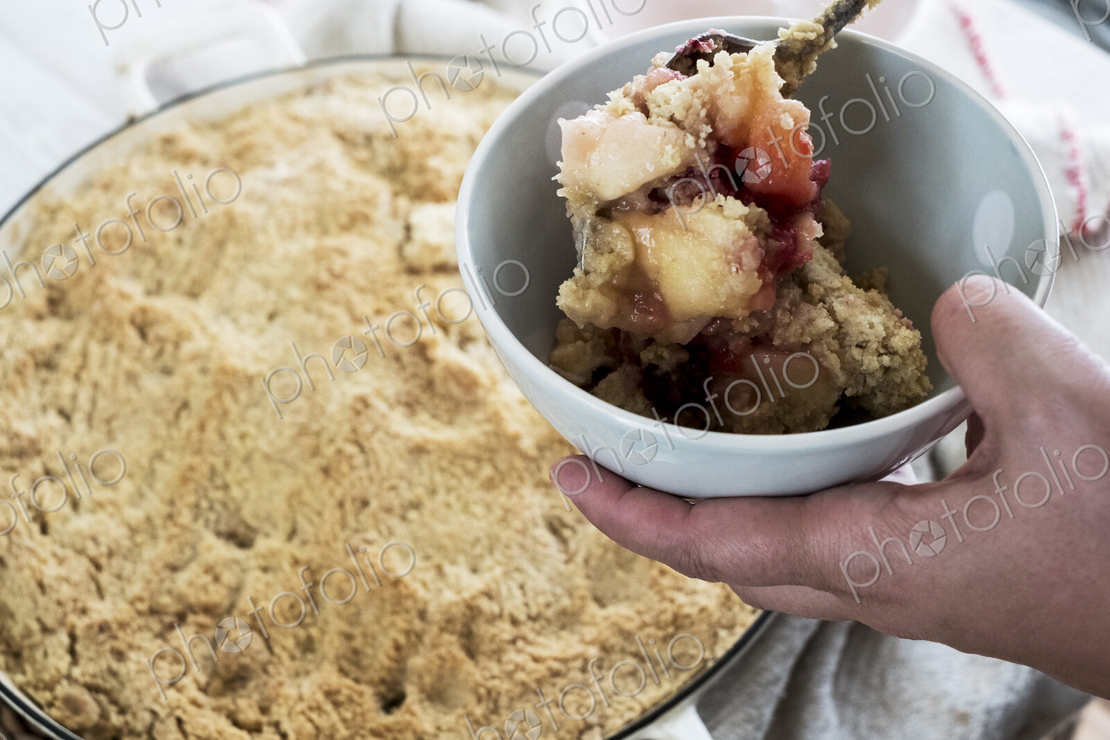 High angle close up of person holding bowl of freshly baked apple and blueberry crumble.