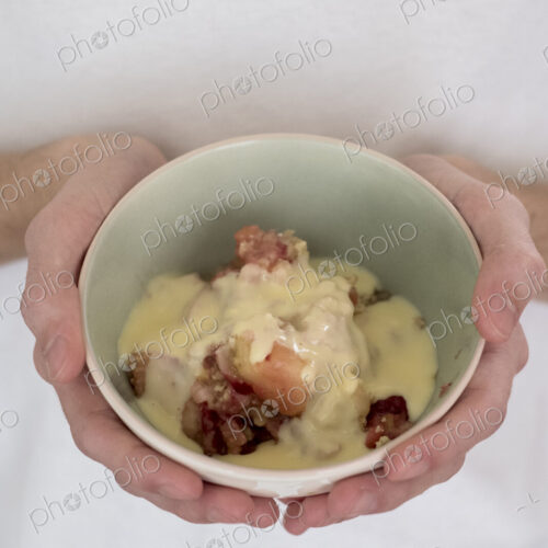 High angle close up of person holding bowl of freshly baked apple and blueberry crumble. High angle close up of person holding bowl of freshly baked apple and blueberry crumble.