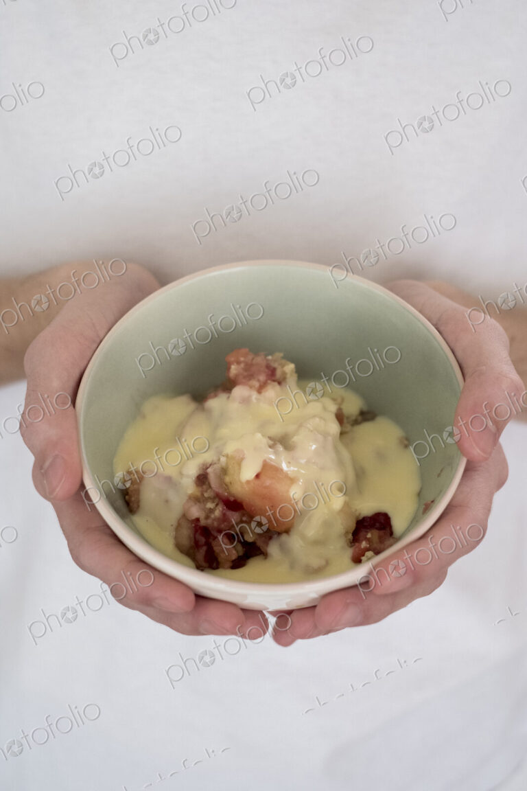 High angle close up of person holding bowl of freshly baked apple and blueberry crumble.