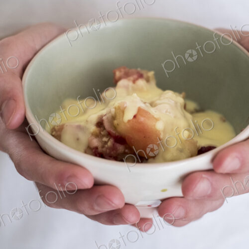 High angle close up of person holding bowl of freshly baked apple and blueberry crumble. High angle close up of person holding bowl of freshly baked apple and blueberry crumble.