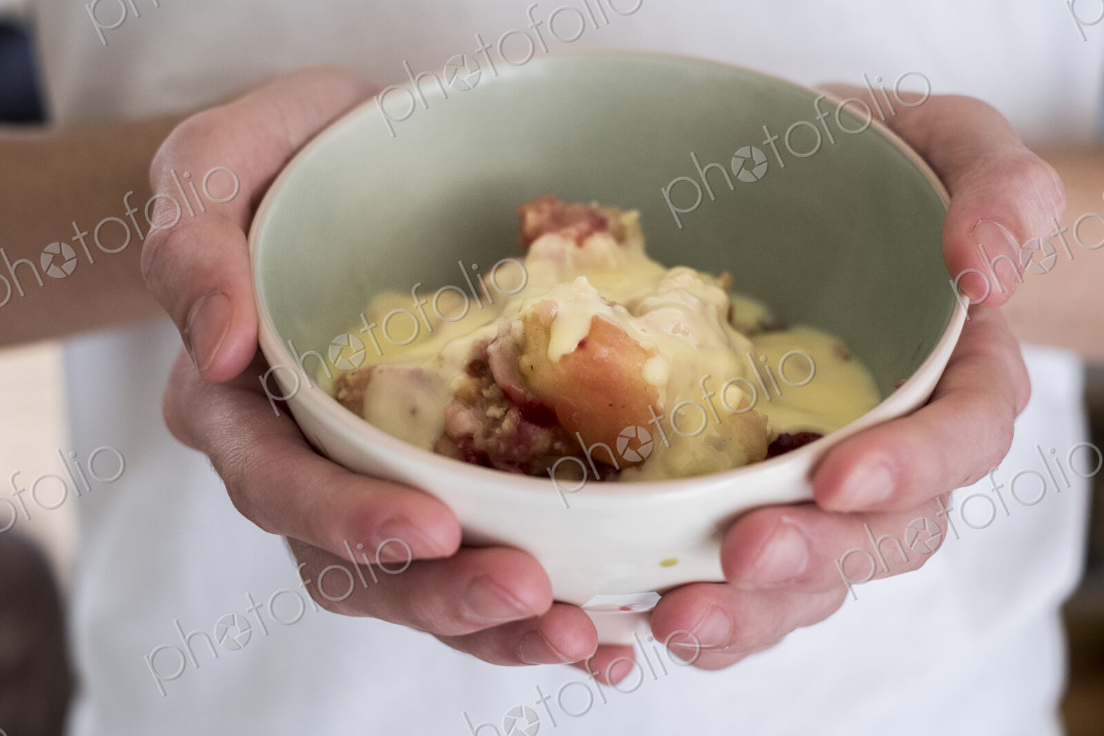 High angle close up of person holding bowl of freshly baked apple and blueberry crumble.