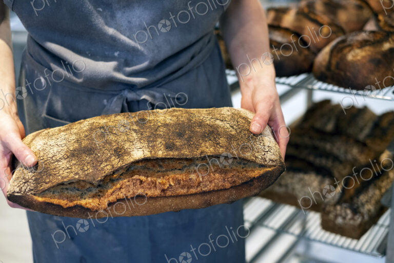 High angle close up of person holding freshly baked loaf of bread in an artisan bakery.