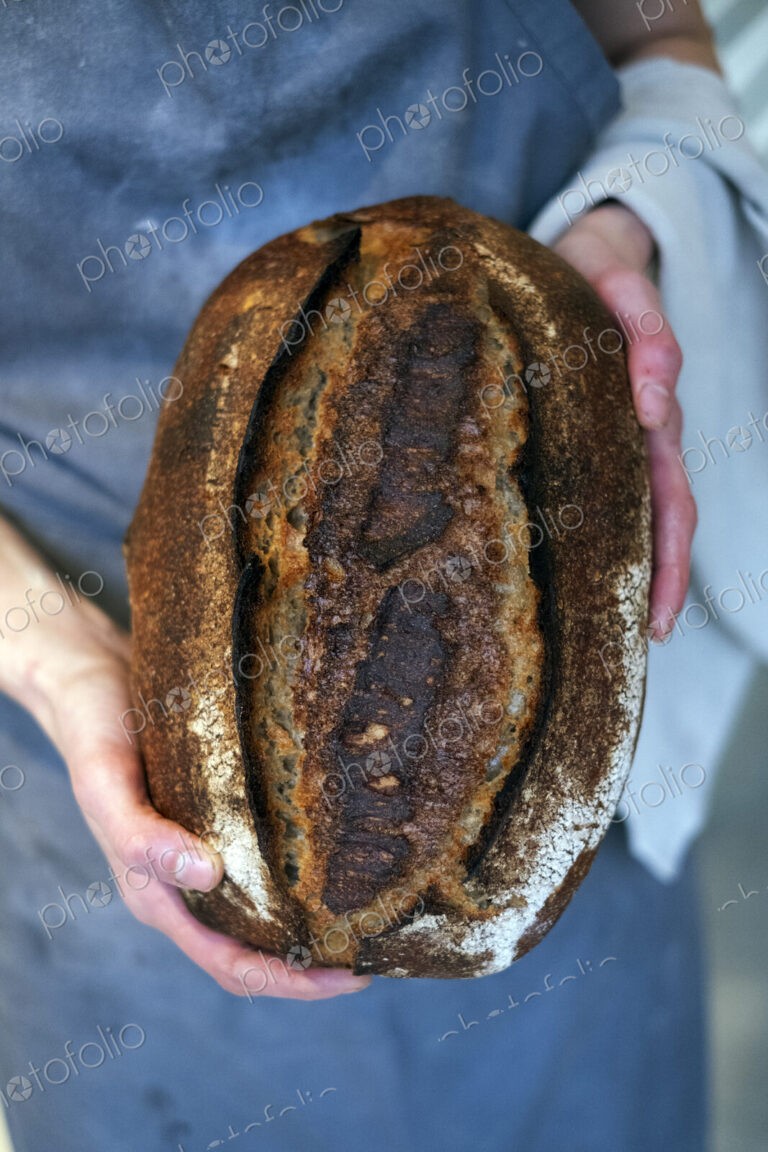 High angle close up of person holding freshly baked loaf of bread in an artisan bakery.