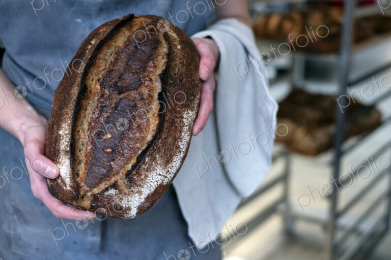 High angle close up of person holding freshly baked loaf of bread in an artisan bakery.