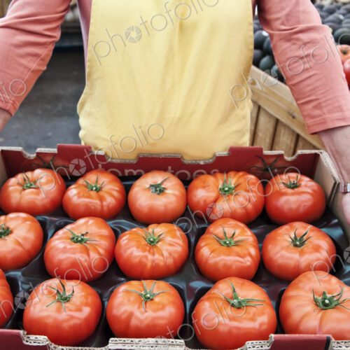 High angle close up of person holding large tray of fresh tomatoes at a fruit and…