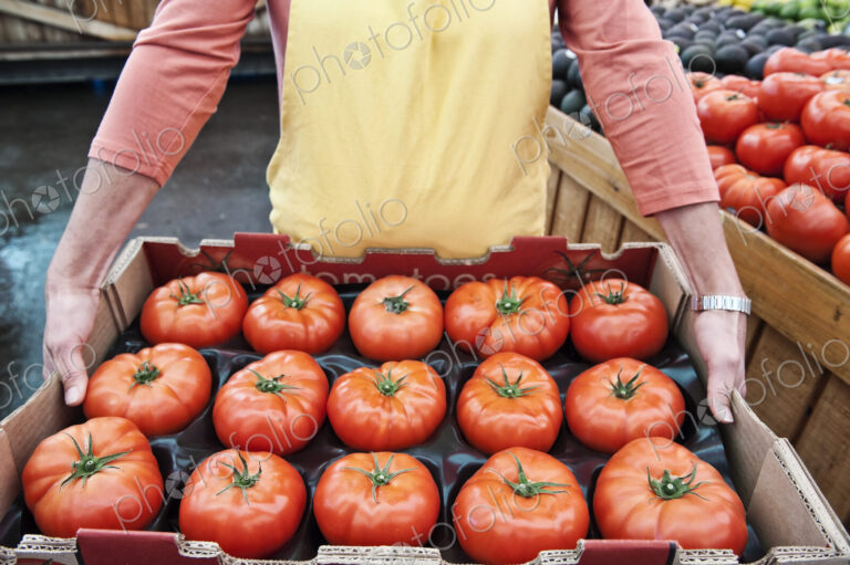 High angle close up of person holding large tray of fresh tomatoes at a fruit and…