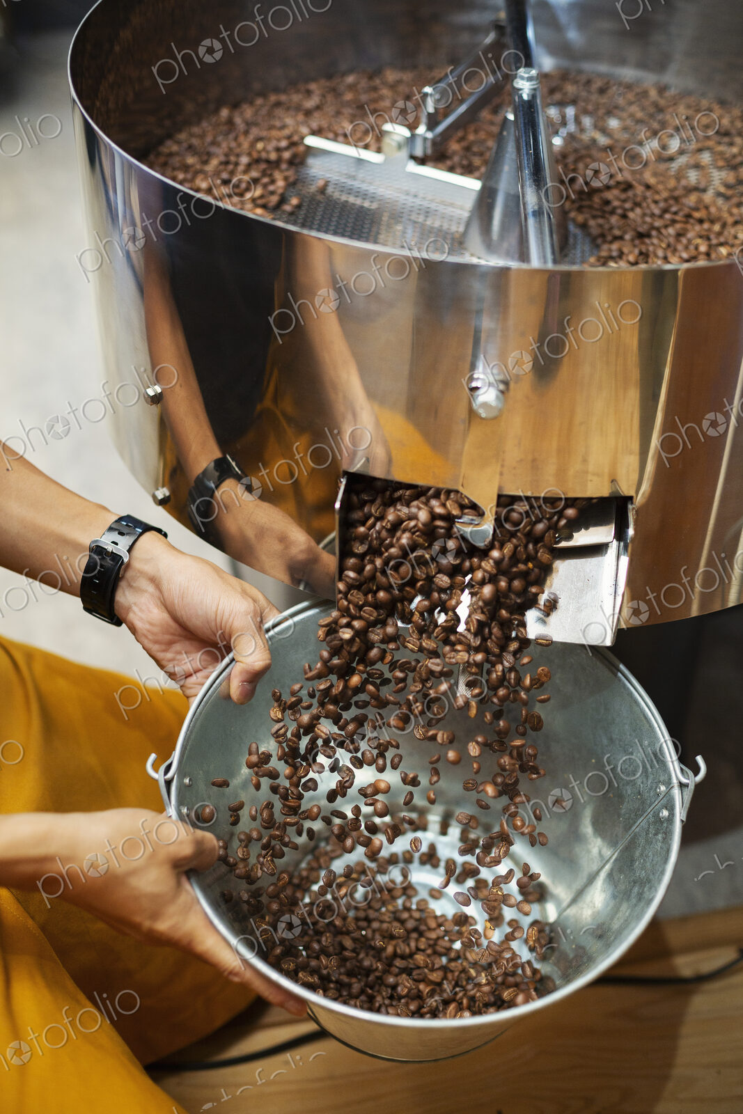High angle close up of person holding metal bucket with freshly roasted coffee beans.