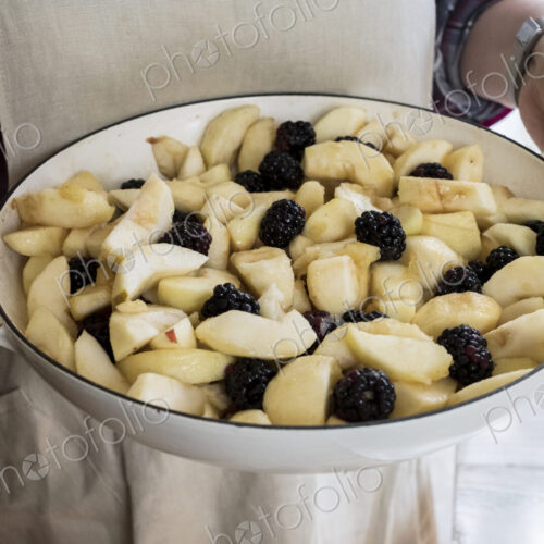 High angle close up of person holding round baking tin with apples and blackberries.