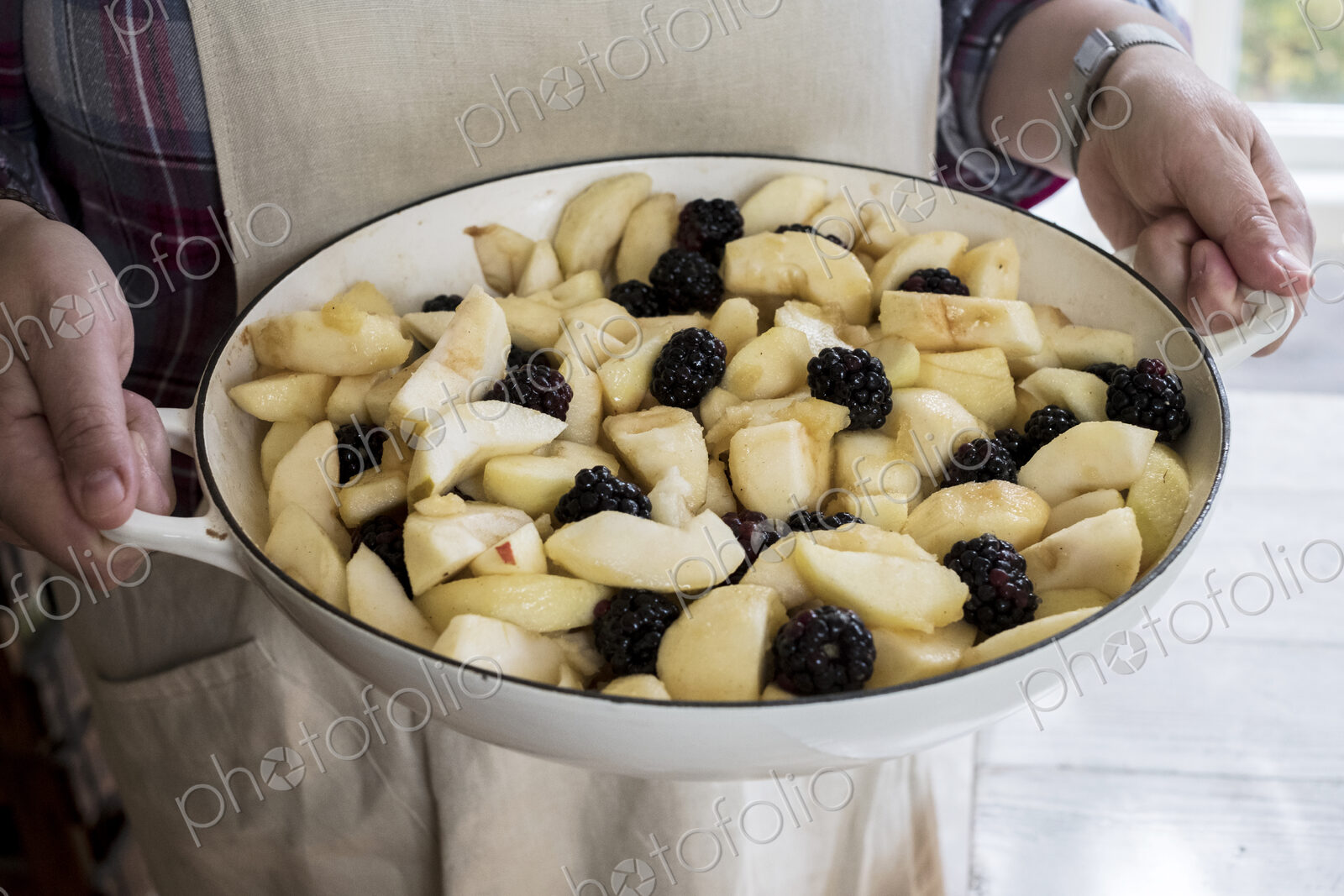 High angle close up of person holding round baking tin with apples and blackberries.