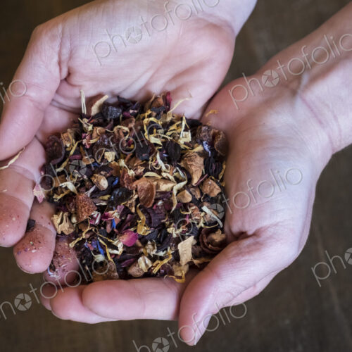High angle close up of person holding small heap of red berry herbal tea infusion.