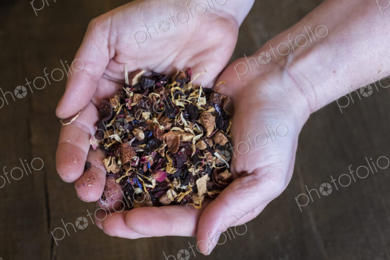 High angle close up of person holding small heap of red berry herbal tea infusion.