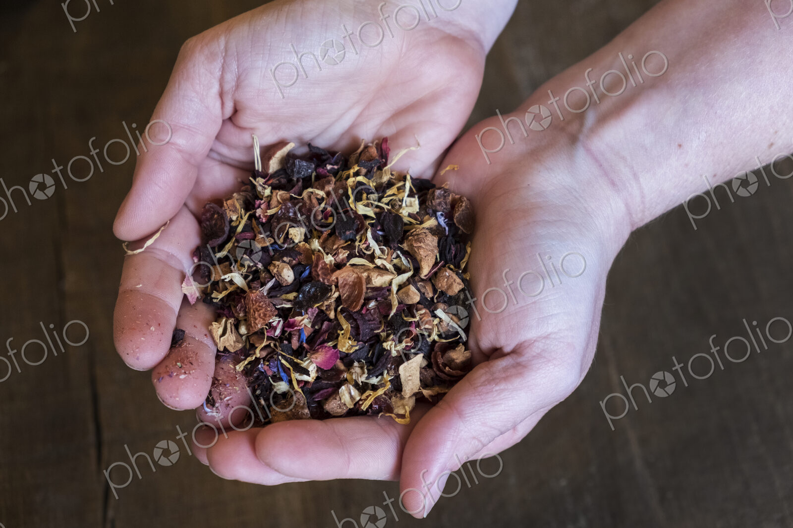 High angle close up of person holding small heap of red berry herbal tea infusion.