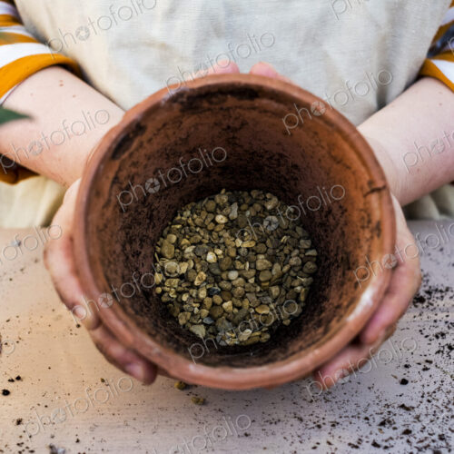 High angle close up of person holding terracotta plant pot with gravel. High angle close up of person holding terracotta plant pot with gravel.