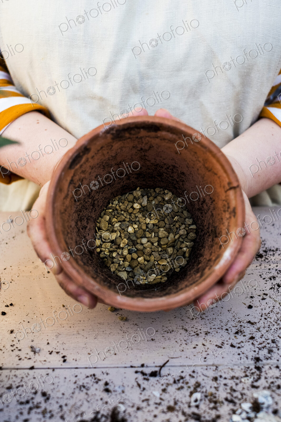 High angle close up of person holding terracotta plant pot with gravel.