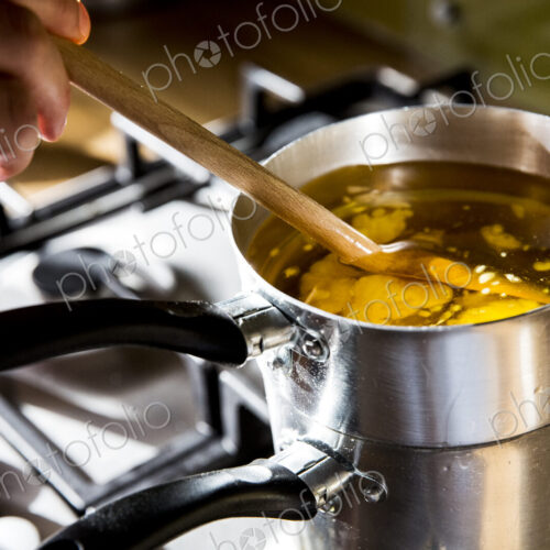 High angle close up of person melting wax for candles in saucepan on stove. High angle close up of person melting wax for candles in saucepan on stove.